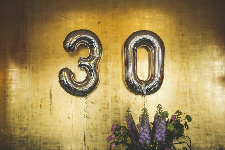 Silver balloons of a "3" and a "0" float against a wood backdrop